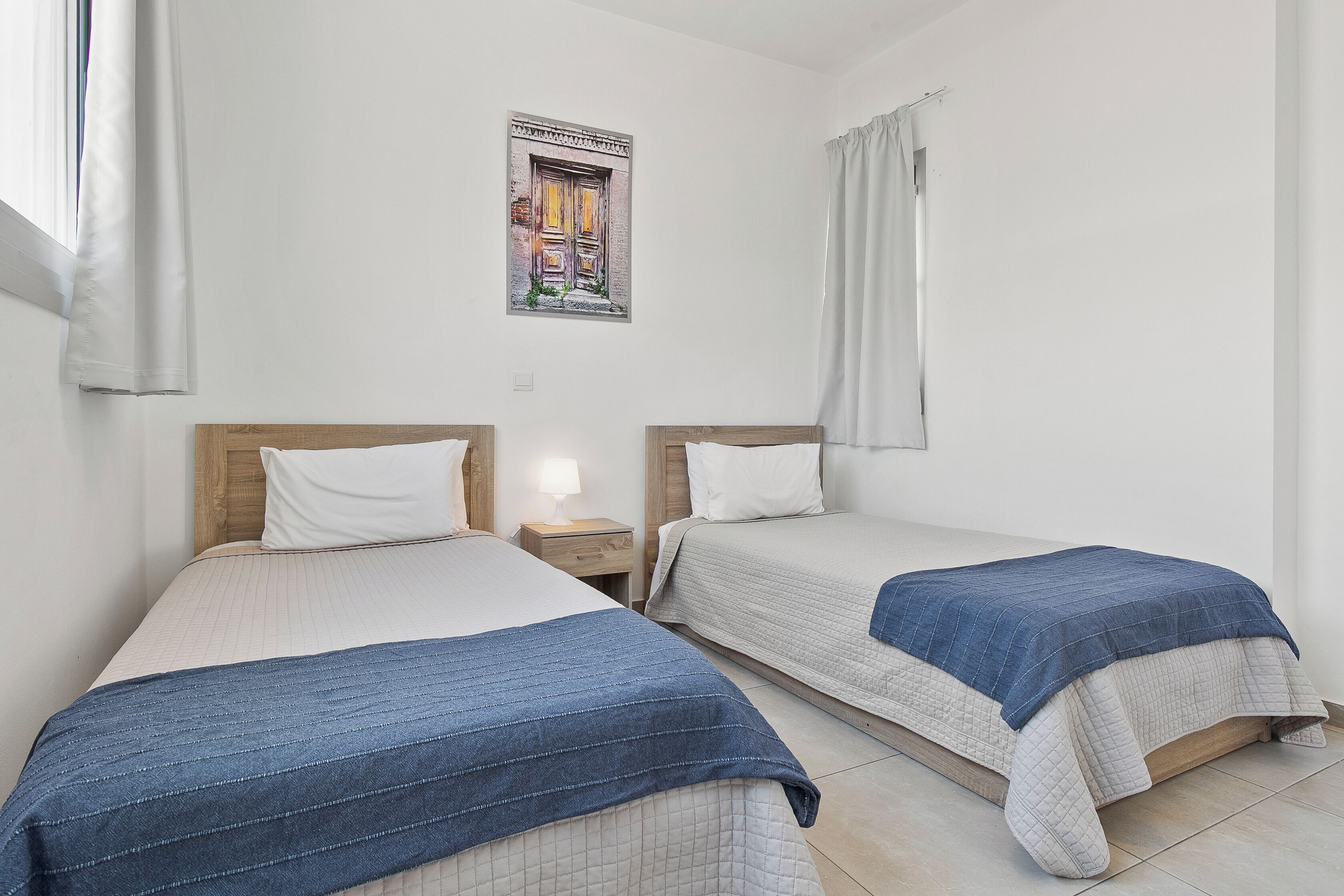 A room with two beds, each with a wooden headboard and white bedding. There is a framed picture on the wall above the beds.