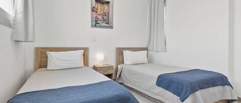 A room with two beds, each with a wooden headboard and white bedding. There is a framed picture on the wall above the beds.