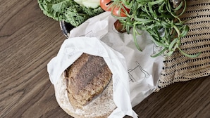Un sac en osier contenant des légumes frais, une miche de pain et un citron, posés sur une surface en bois.