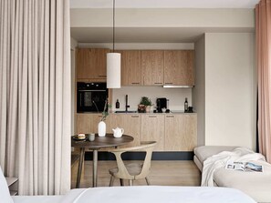 Une chambre d’hôtel moderne dotée d’un coin repas, d’une kitchenette et d’un lit avec un magazine.