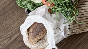 Una cesta de mimbre con verduras frescas, una hogaza de pan y un limón sobre una superficie de madera.