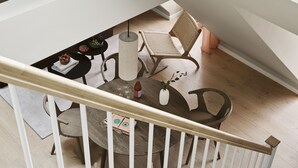Ett modernt vardagsrum i loftstil med högt i tak, en matplats med ett runt bord och stolar, en flätad stol och en trappa med ett träräcke.