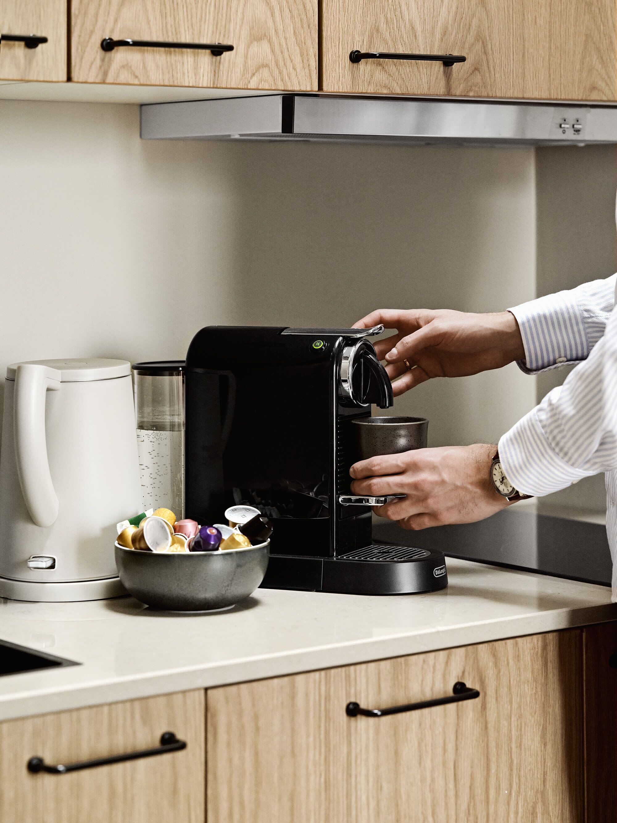 A person using a coffee machine in a kitchen with wooden cabinets and a stainless steel range hood.