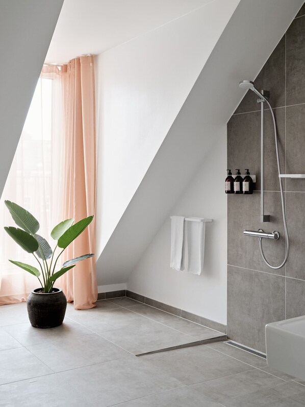 A modern bathroom with a shower, a potted plant, and a towel rack.