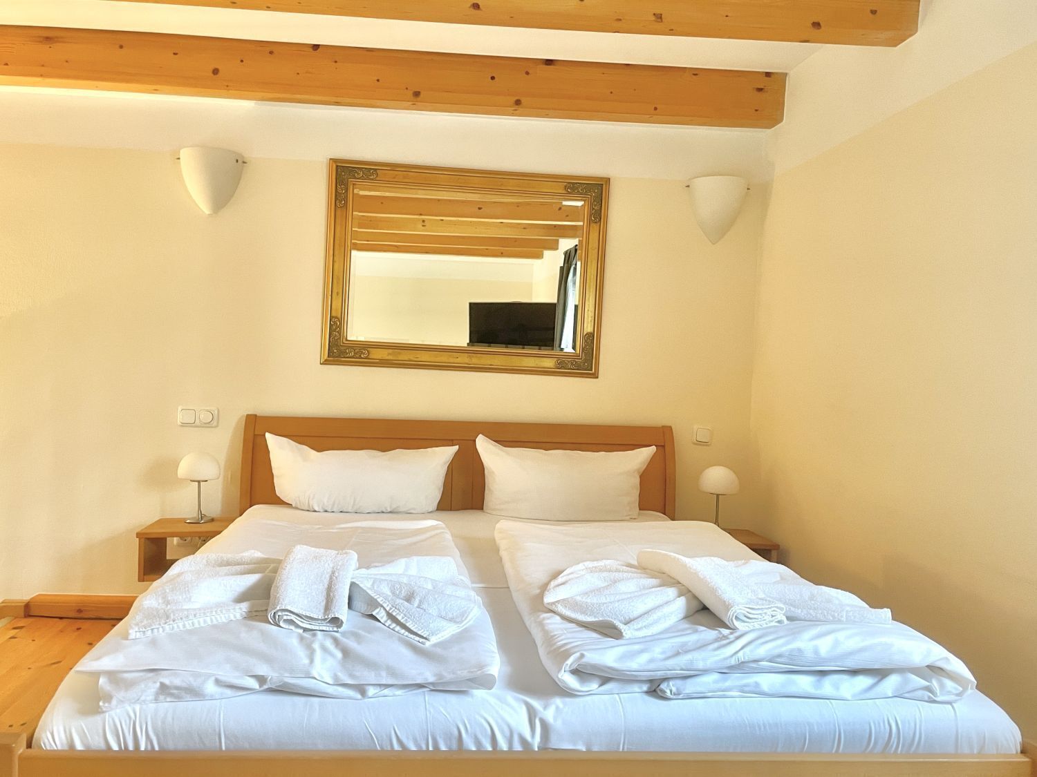 Ein Doppelbett mit weißen Leinen und Handtüchern, ein Holz-Kopfteil, ein großer Spiegel und Nachttischlampen.