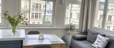 A modern living room with a dining area, large windows, and a view of neighboring buildings.