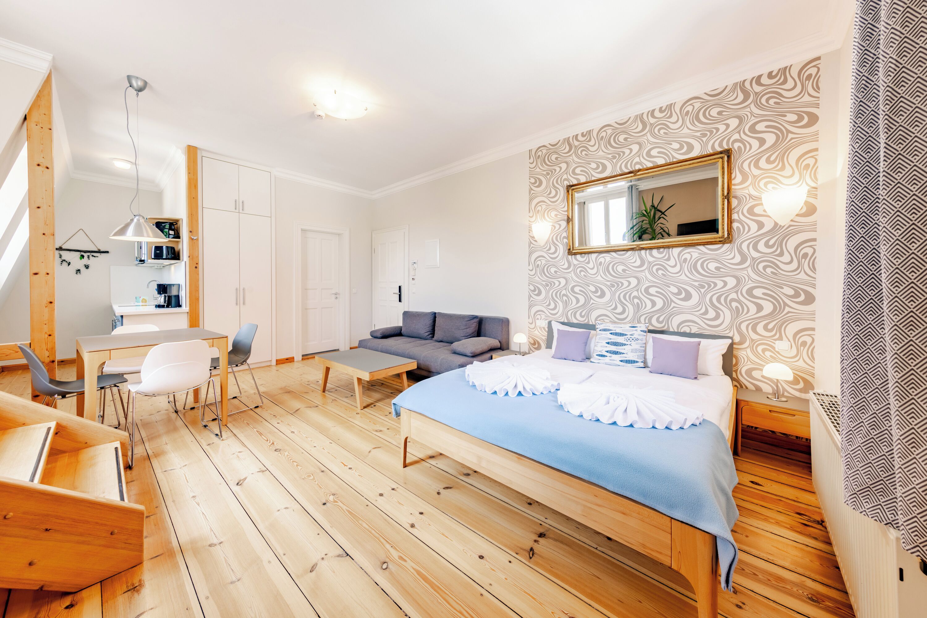 A bedroom with a bed, a sofa, a desk, and a chair. There is a mirror on the wall and a plant on the desk.