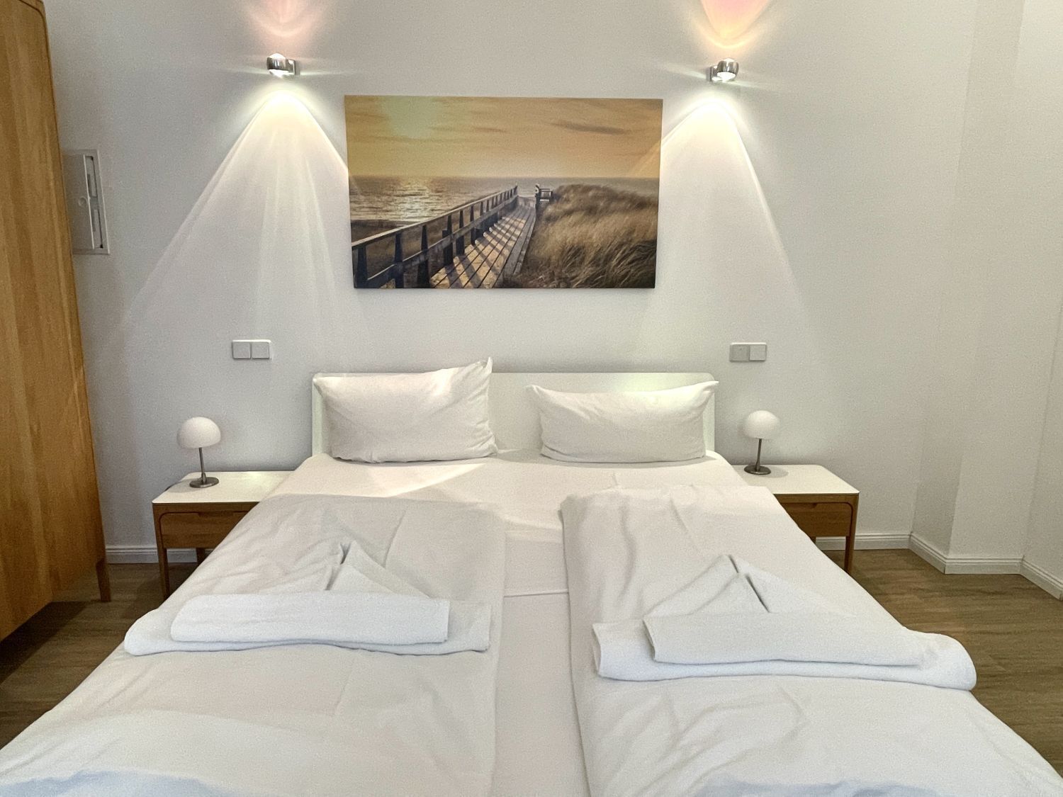 Habitación de hotel con dos camas, un cuadro de un muelle y dos lámparas de noche.
