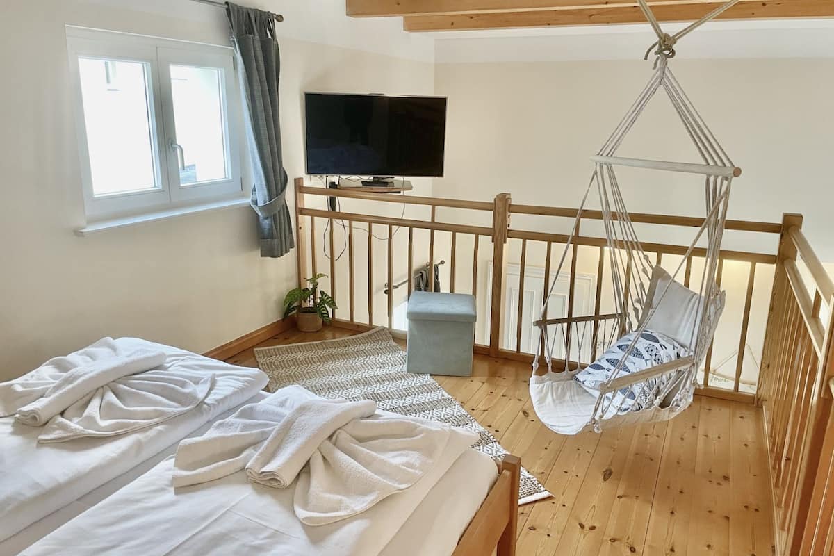 A bedroom with a bed, a hanging chair, a TV, and a window.