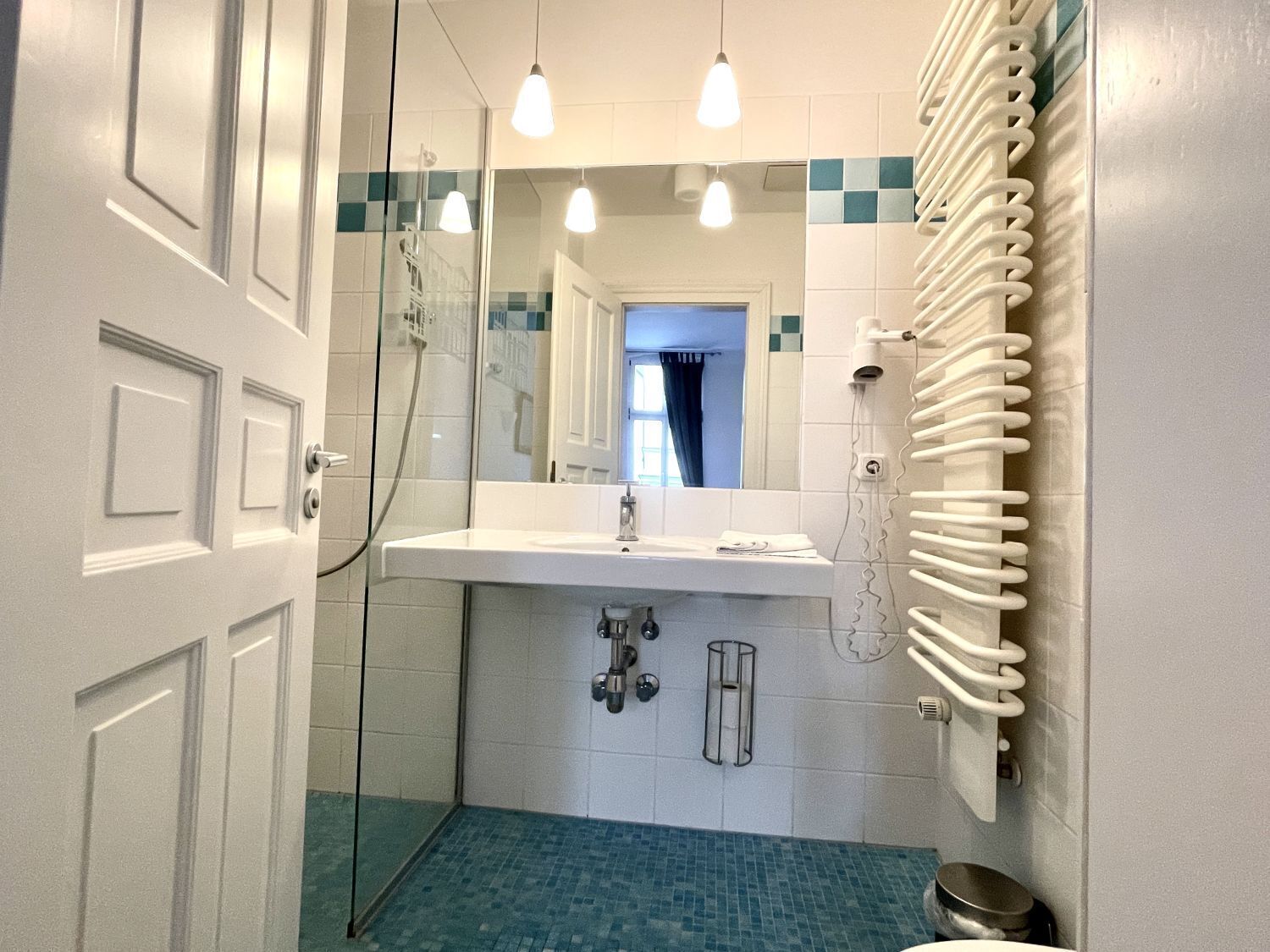 Un baño con cabina de ducha de vidrio, un lavamanos blanco con un espejo encima y un perchero en la pared.