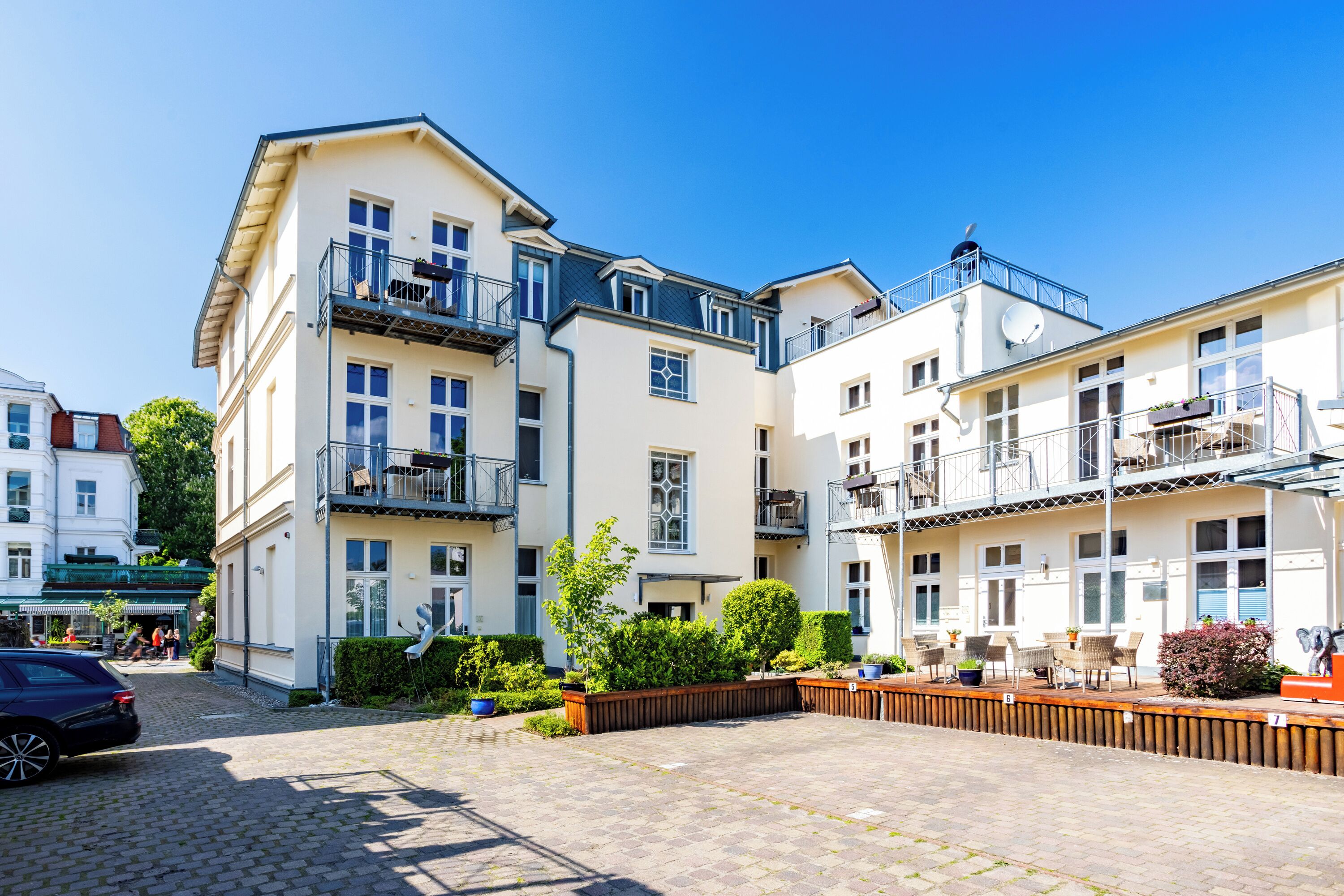 Ein mehrstöckiges Wohngebäude mit Balkonen, einem gepflasterten Innenhof und Sitzgelegenheiten im Freien.