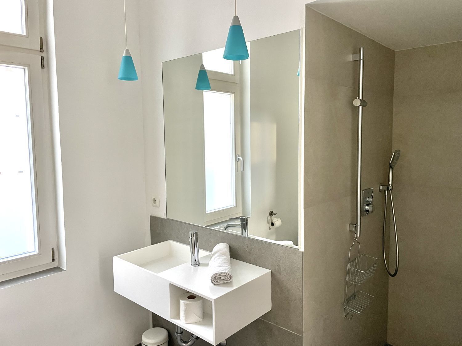 Une salle de bain moderne avec un lavabo blanc, un grand miroir et une douche.