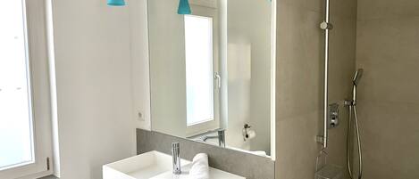 Une salle de bain moderne avec un lavabo blanc, un grand miroir et une douche.