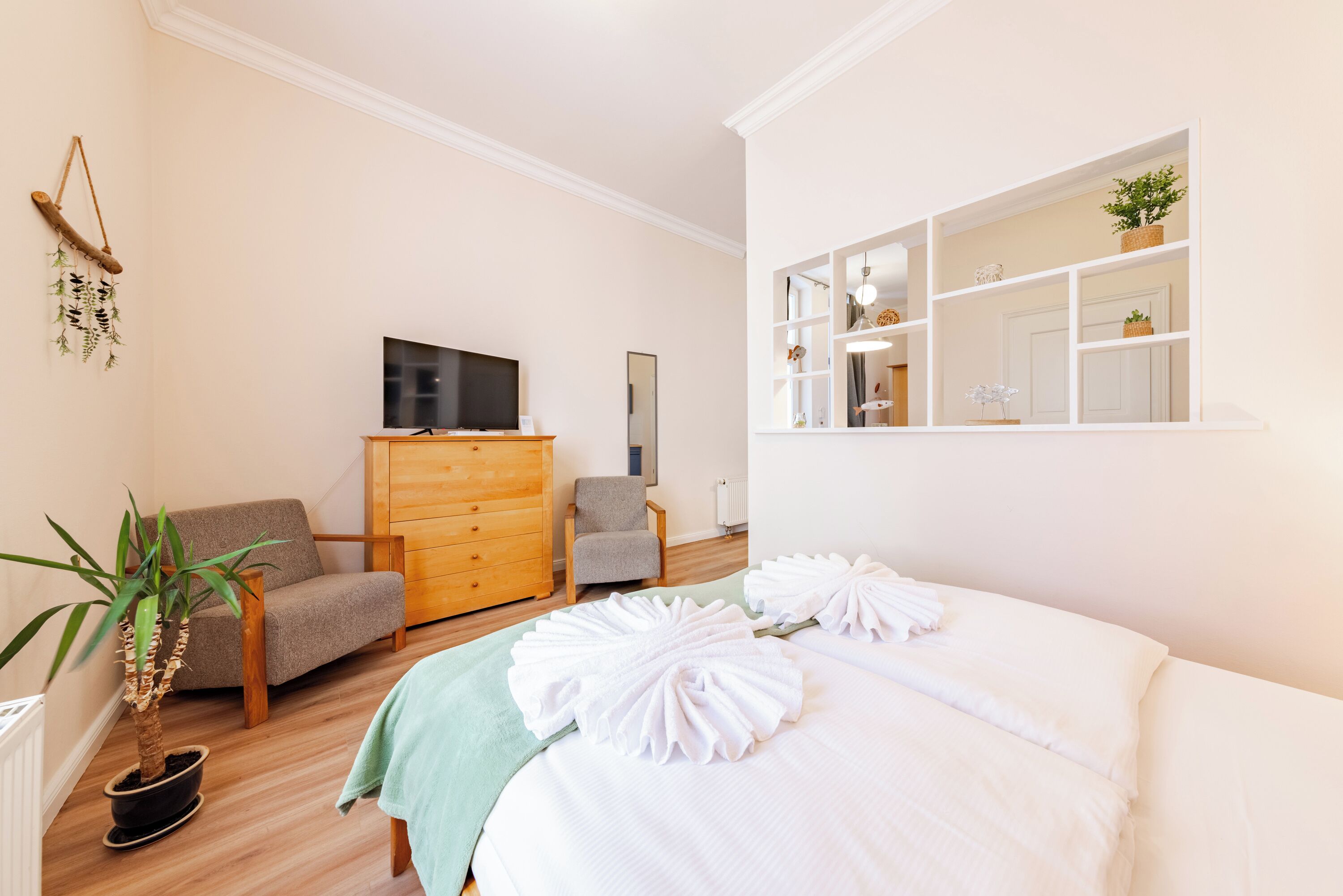 A hotel room with a bed, a TV, a dresser, a chair, and a potted plant.