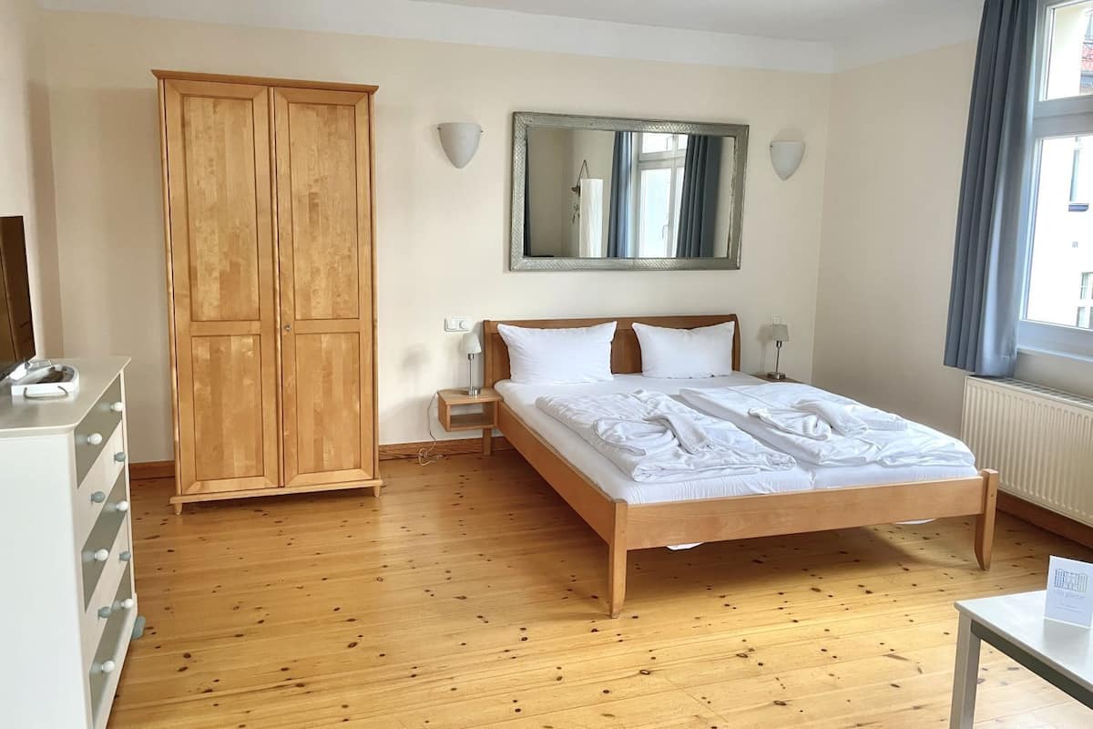 A hotel room with a wooden bed, a wardrobe, a mirror, and a window with curtains.