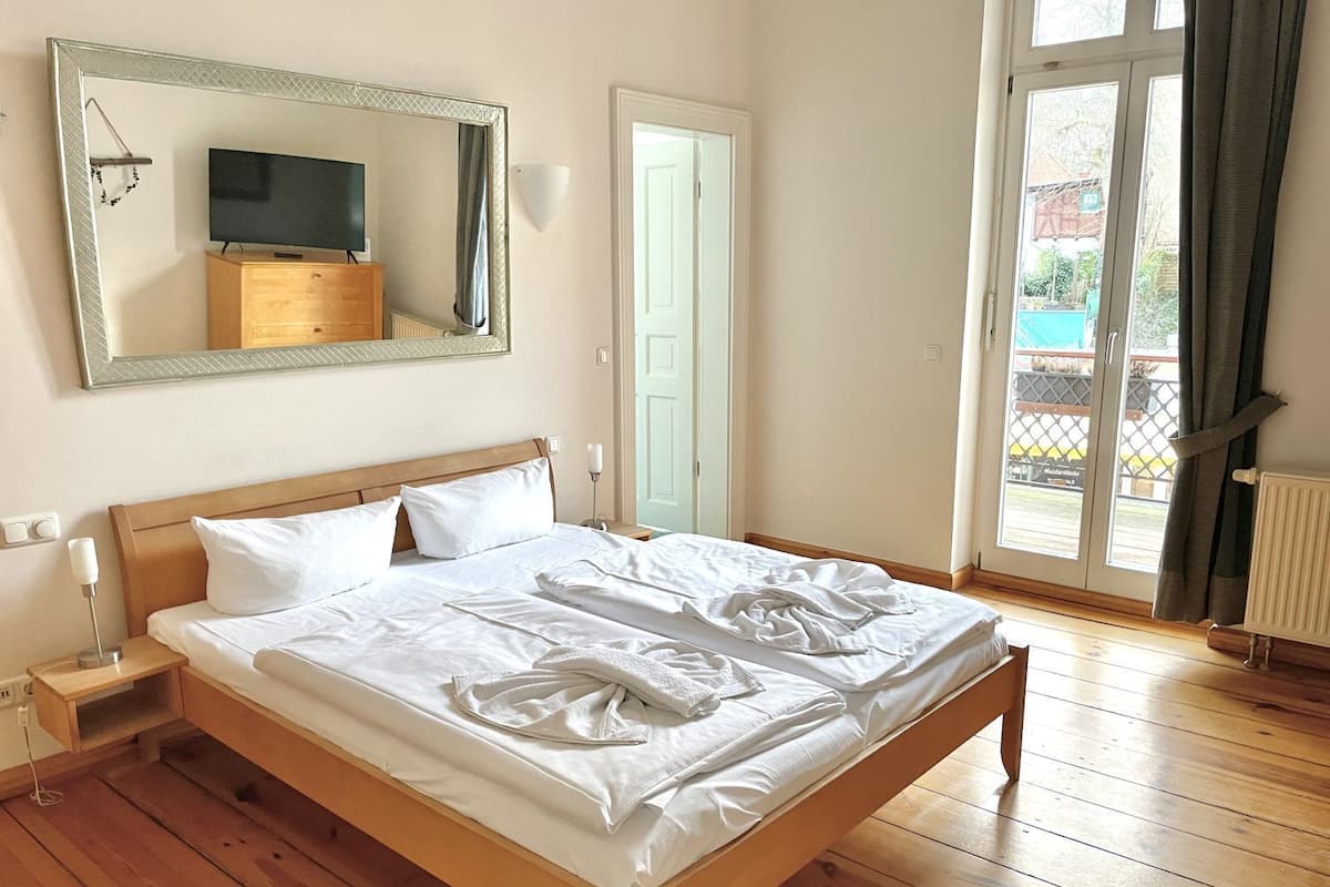 A hotel room with a wooden bed, a large mirror, a television, and a view of the outside.