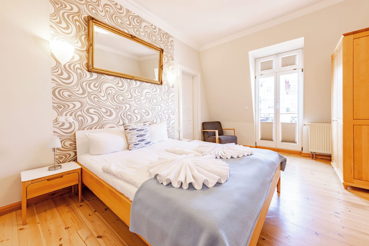 A bedroom with a large bed, a nightstand, a chair, and a wardrobe.