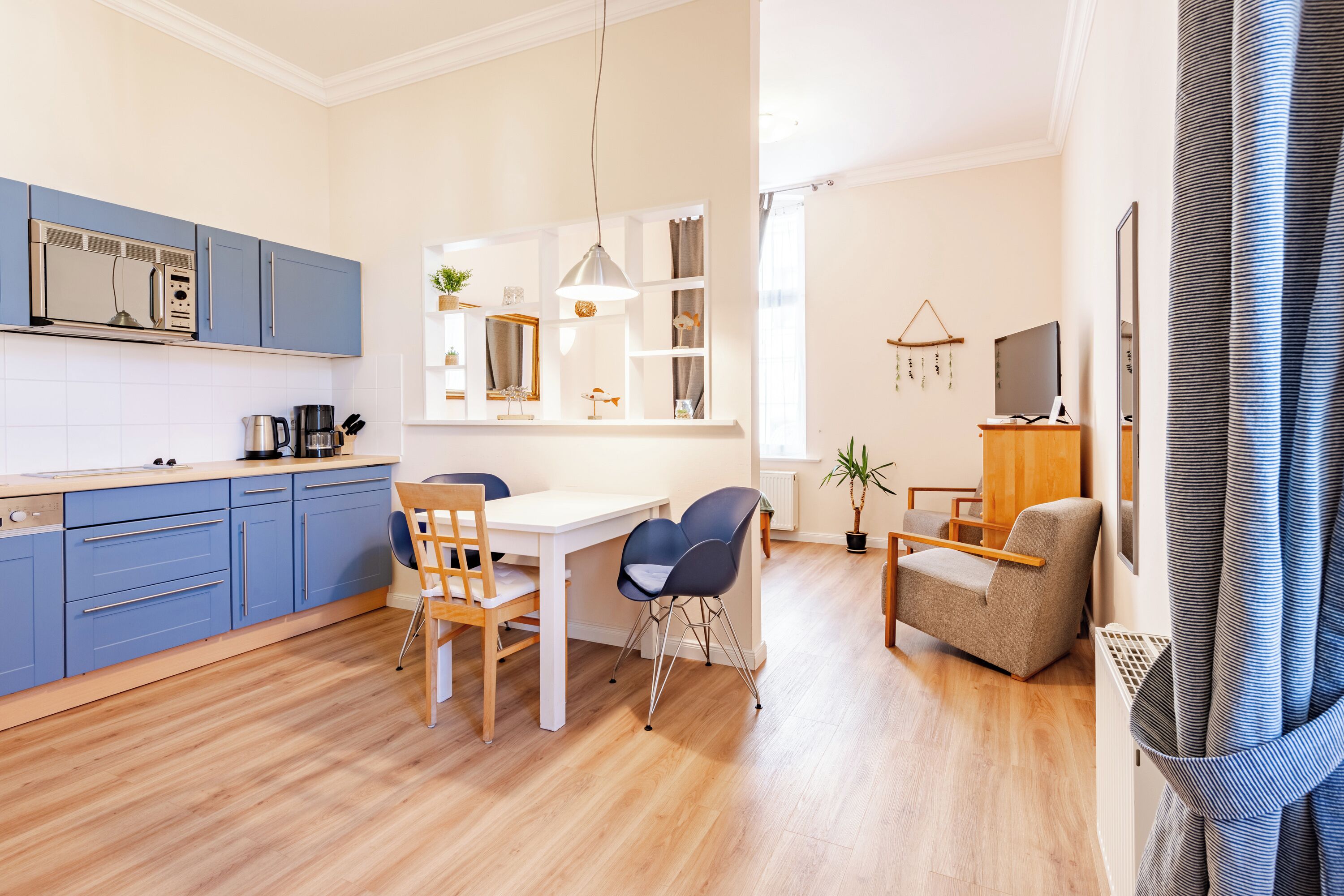 Een moderne keuken met blauwe kastjes, een witte eettafel en een bank.