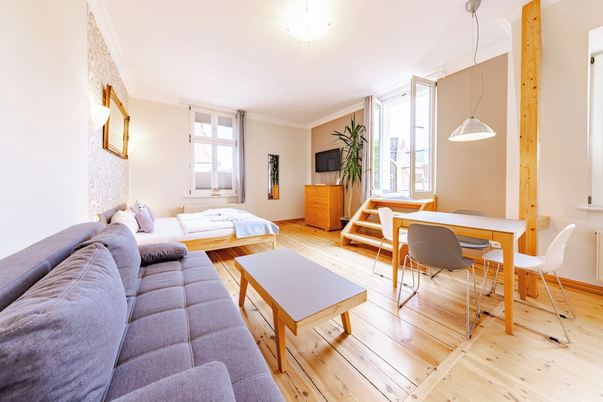 A modern living room with a grey sofa, wooden coffee table, and a dining area with a table and chairs.