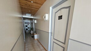 Un couloir avec un plafond en bois, une porte avec une pancarte et une vue sur une pièce où l’on peut voir une autre pancarte indiquant « MAISON ».
