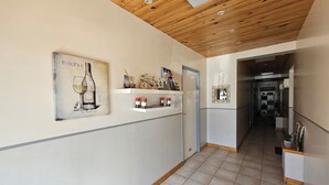 Un couloir avec un plafond en bois, une œuvre d’art encadrée représentant une bouteille de vin, et des étagères remplies de livres et de bocaux.