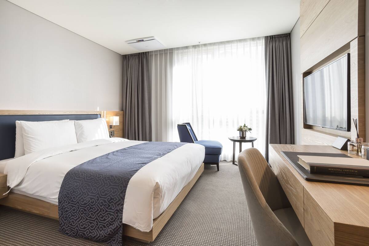 A hotel room with a large bed, a desk with a chair, a television, and a window with curtains.