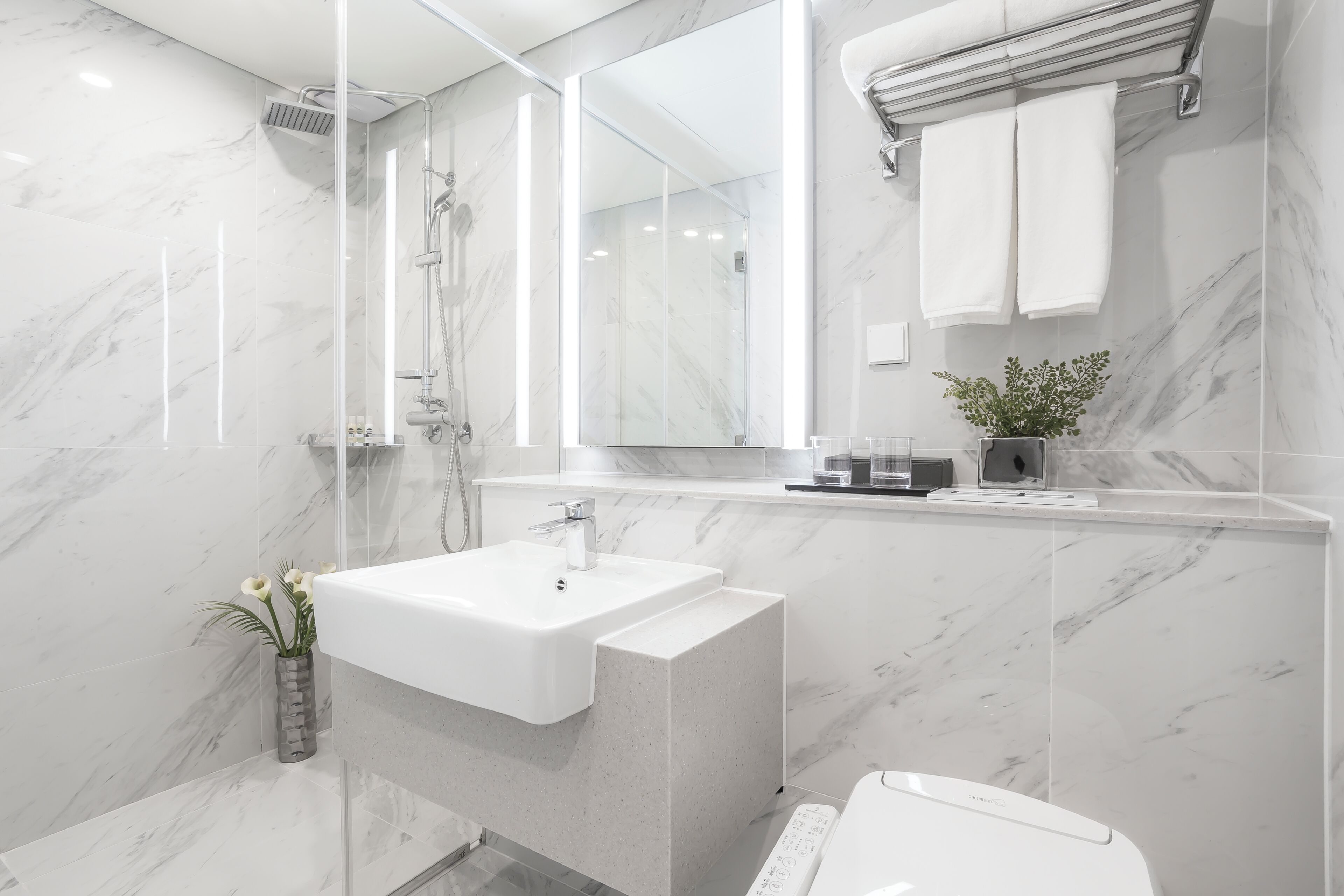 Ein modernes Badezimmer mit einem мраморной Waschbecken, einer Duschkabine aus Glas und einem großen Spiegel.