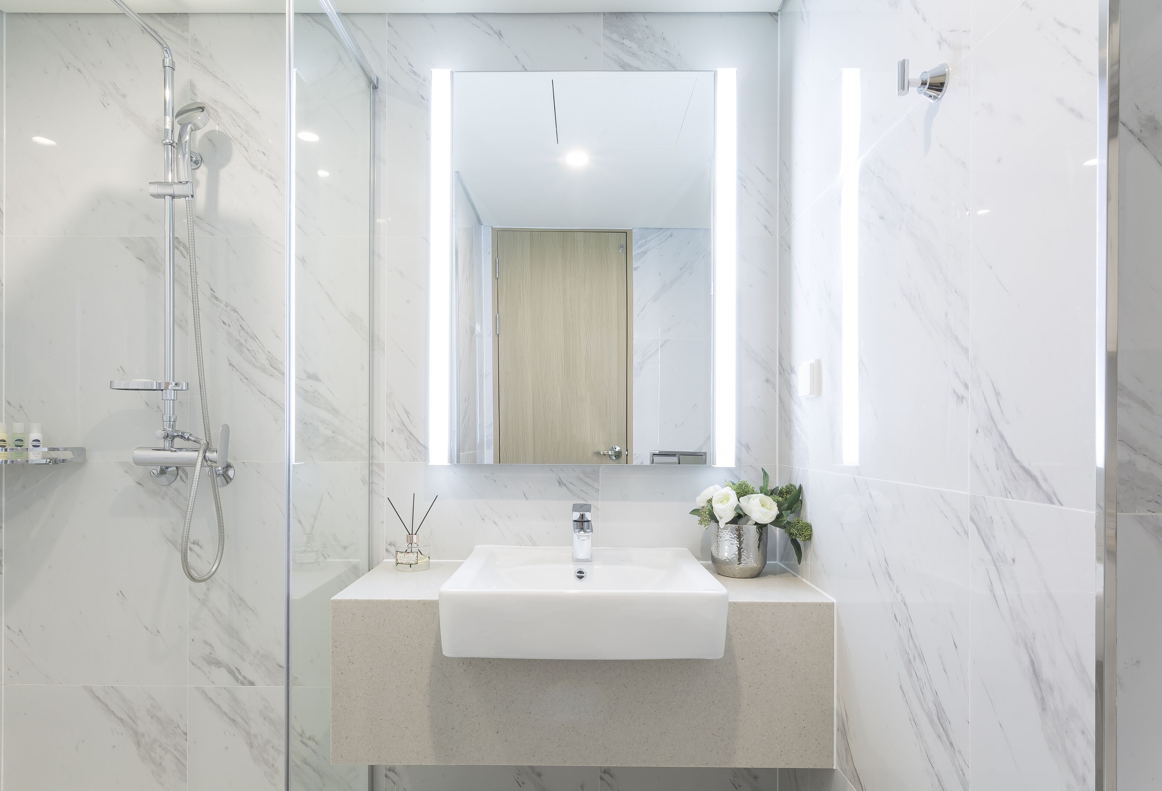 Een moderne badkamer met een douchecabine van glas, een betegelde wand van marmer, een wit wastafelmeubel en een spiegel erboven.