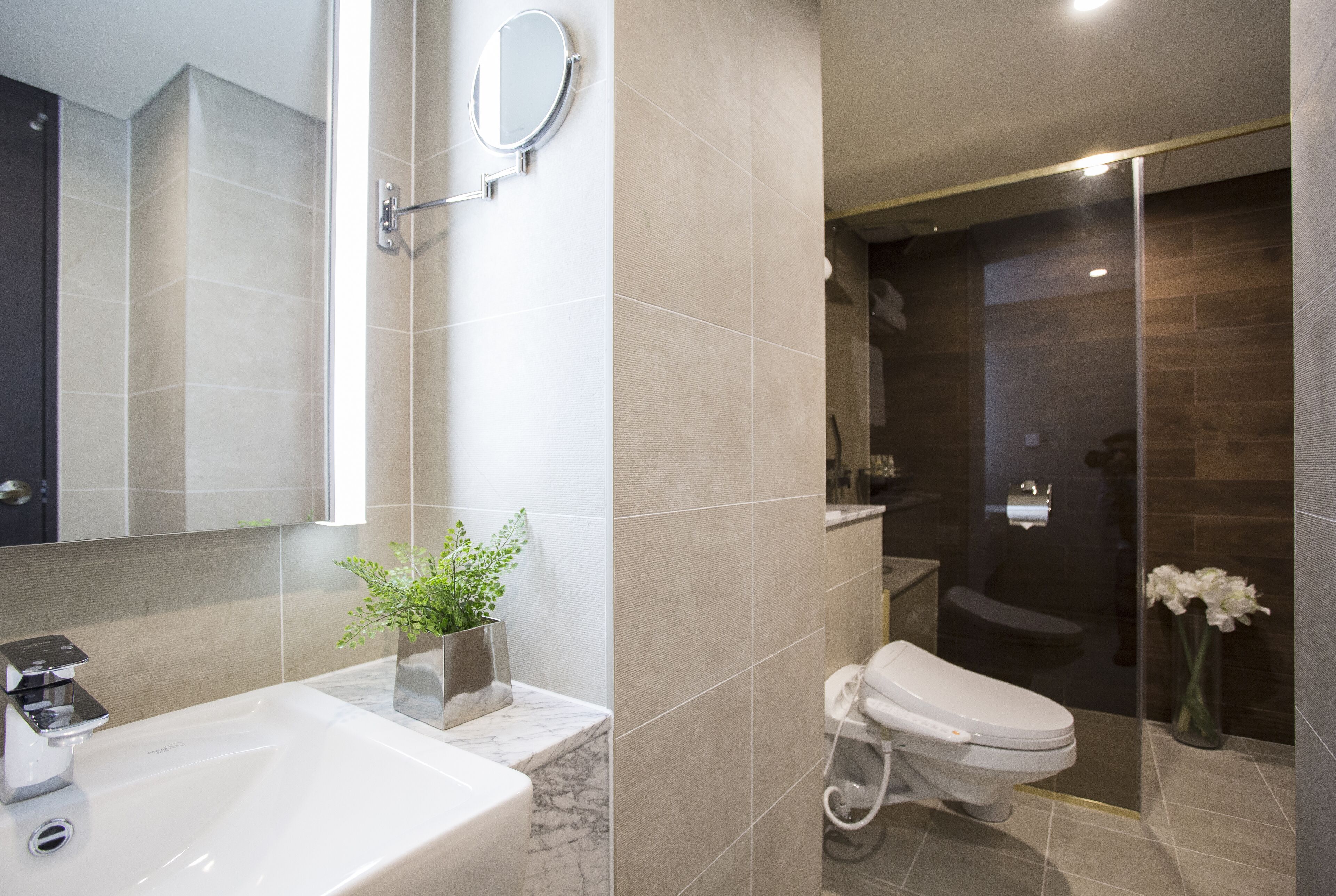 A modern bathroom with a marble sink, a toilet, a shower area, and a large mirror.