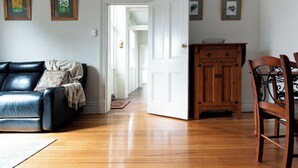 A living room with a black leather sofa, wooden cabinet, and metal chair. A white door leads to another room. - Timeless Treasure: Near the City Centre & WiFi (Launceston)