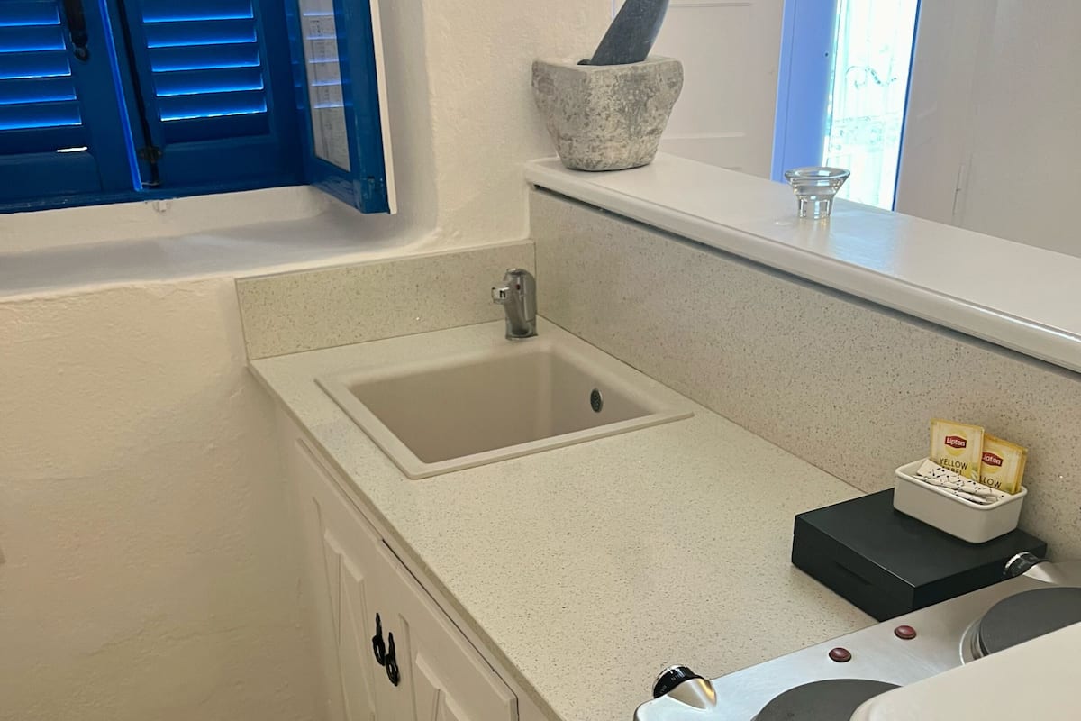 A kitchen with a sink, a stone mortar, a toaster, and a window with blue shutters.