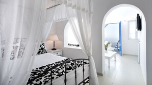 A bedroom with a canopy bed, a bedside table with a lamp, and a view of the outside through an arched doorway. - Artemis Villas (Santorini)