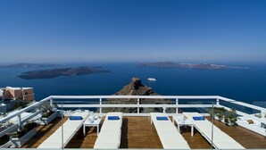 A rooftop terrace with white lounge chairs, a wooden deck, and a view of the sea and islands. - Artemis Villas (Santorini)