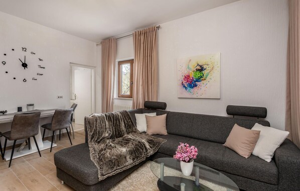 A modern living room with a grey sofa, a furry throw blanket, and a glass coffee table with a vase of pink flowers.