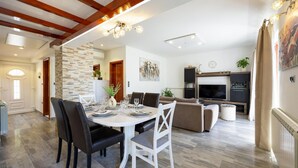 A modern living room with a fireplace, a dining area with a white table set, and a kitchen area with dark cabinets.
