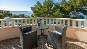 A balcony with wicker chairs and a table, overlooking a body of water and trees.