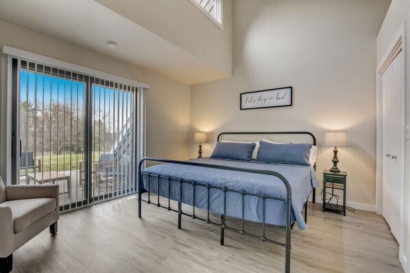 A bedroom with a bed, a chair, a nightstand, a lamp, and a sliding glass door leading to a patio.