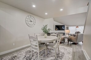 A modern living room with a dining area, featuring a round table, chairs, a clock, a plant, and a sofa. - The Getaway at Tamarack (Wisconsin Dells)