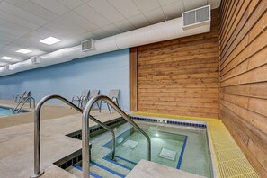 Una piscina interior amb aigua cristal·lina, baranes de metall i una paret de fusta.