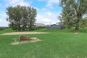A grassy outdoor area with trees, a fenced area, and a building in the background.
