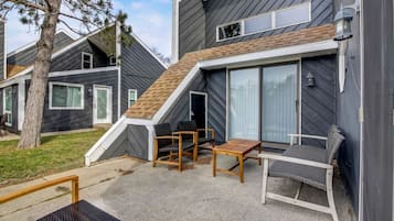 Un edificio moderno de dos pisos con techo inclinado, un patio cubierto con mobiliario exterior y un amplio ventanal corredizo.