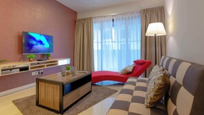 Un soggiorno moderno con una TV a schermo piatto, una poltrona rossa, un divano a righe e un'ampia finestra con tende leggere.