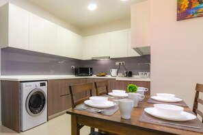 Cocina compacta con lavadora, microondas y mesa de comedor con vajilla y tazas blancas.