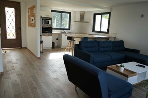 A modern living room with a sectional sofa, a dining table, and a kitchen area with a microwave and stove. - Maison Contemporaine aux Portes de Brest (BOHARS)