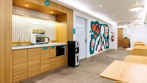 A modern kitchen with a coffee machine, a water dispenser, and a microwave. There are wooden cabinets and a tiled backsplash. - Bobopod Thamrin, Jakarta (Jakarta)