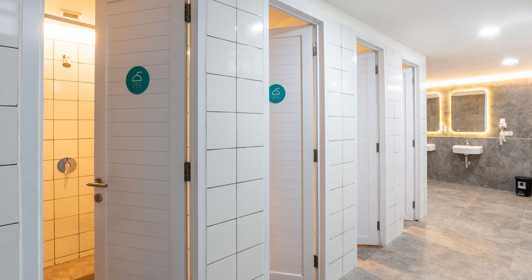 A modern bathroom with multiple shower stalls, each marked with a wheelchair accessibility sign, and a sink area with a mirror.