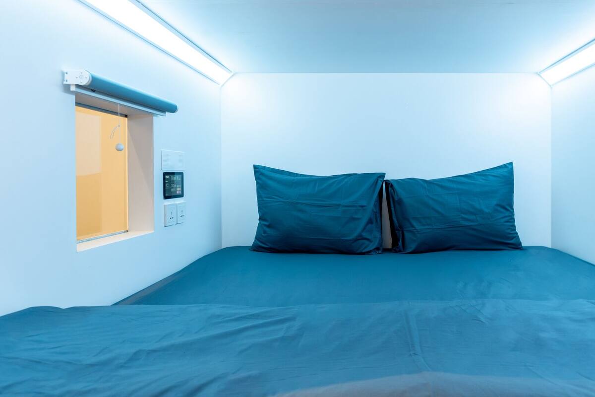 Ein kleines, modernes Schlafzimmer mit einem Einzelbett, einem Fenster mit Blick und einer Bedienkonsole an der Wand.