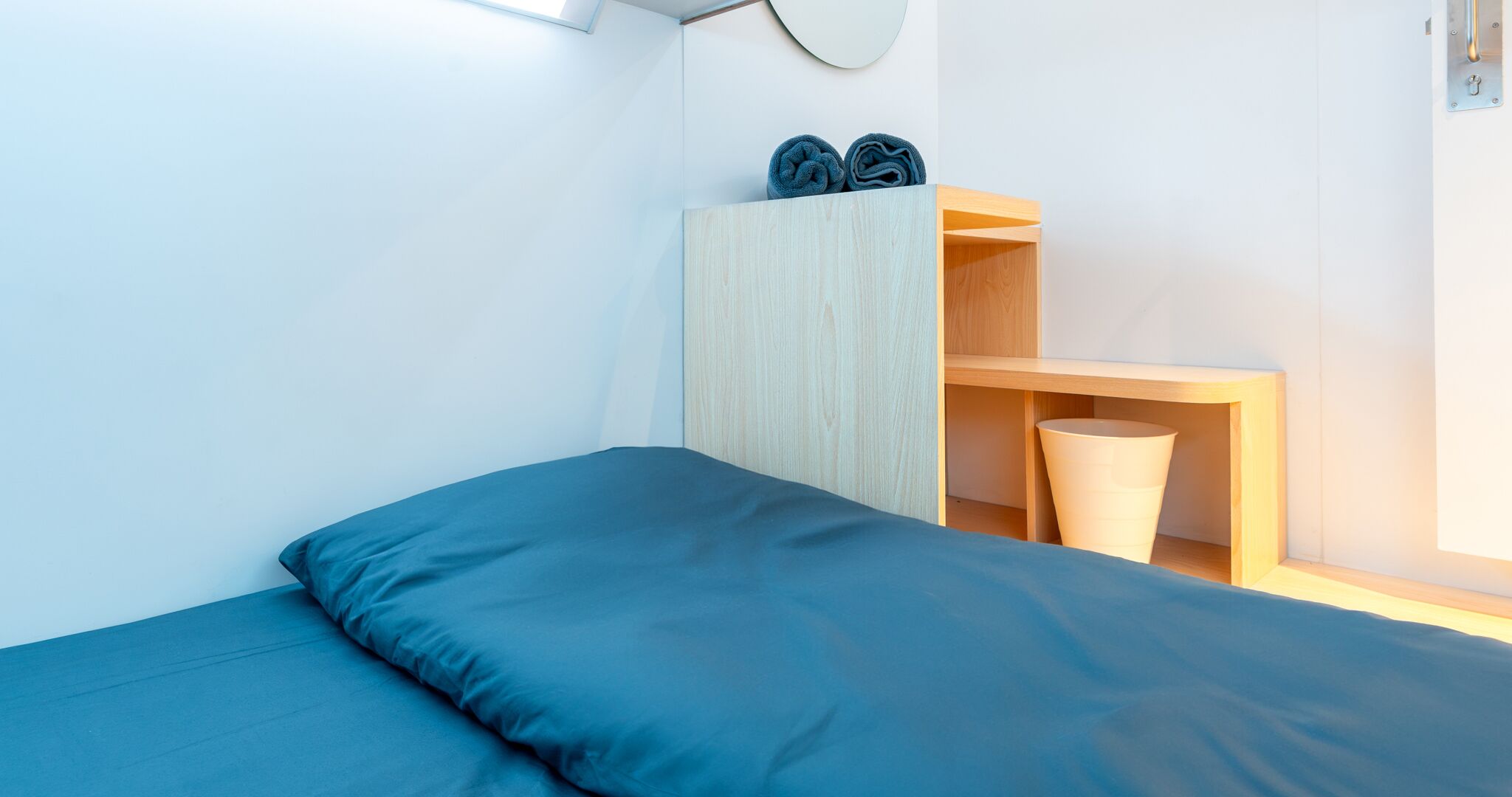 Ein kleines, ordentlich eingerichtetes Schlafzimmer mit einem Bett, einer Holzhilfe für Handtücher und einer kleinen Kommode.