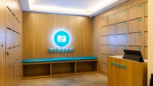 A modern locker room with wooden lockers, a blue bench, and a reception desk with a logo. - Bobopod Thamrin, Jakarta (Jakarta)