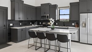 A modern kitchen with dark cabinetry, a central island with bar stools, a built-in microwave, and a refrigerator. - Vizcaya #2 - Moab's Newest Luxury Rental (Hot Tub) (Moab)